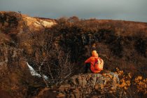 Вид ззаду молодого туриста в зимовому одязі, який дивиться на каскад і гірську річку між кам'яним пагорбом — стокове фото