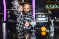 Focused maschio barista aggiungendo liquido dalla bottiglia in jigger mentre si prepara cocktail in piedi al bancone in bar moderno — Foto stock