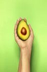 Crop unrecognizable female demonstrating delicious cut ripe avocado with soft pulp on bright green background — Stock Photo