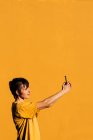 Mulher contemporânea com corte de cabelo elegante e piercing usando smartphone em mídias sociais contra fundo amarelo — Fotografia de Stock