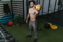Athletic male with naked torso doing exercises with heavy kettlebell during active training in sports center — Stock Photo