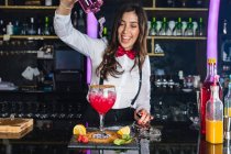 Konzentrierte Barkeeperin in stylischem Outfit, die Flüssigkeit aus der Flasche ins Glas gibt, während sie an der Theke in einer modernen Bar Cocktails zubereitet — Stockfoto