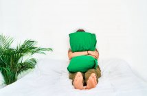 Volle Länge der nicht wiederzuerkennenden unglücklichen Frau umarmt grünes Kissen, während sie allein zu Hause auf dem Bett sitzt — Stockfoto