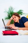 Positive young female freelancer in casual clothes lying down on bed and typing on laptop while working on remote project at home — Stock Photo