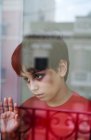 Durch das Glas eines unglücklichen Jungen mit blauen Flecken im Gesicht, der wegschaut, während er am Fenster zu Hause steht, als Begriff häuslicher Gewalt und Kindesmissbrauch — Stockfoto