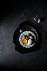 De arriba composición de huevos de gallina crudos en platos y huevos de codorniz en el nido sobre fondo negro - foto de stock
