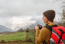 Вид сбоку женщины с рюкзаком, фотографирующей горный пейзаж во время путешествия — стоковое фото