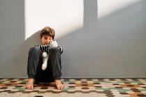 Bouleversé solitaire préadolescent garçon victime de violence domestique assis sur le sol et embrasser jouet — Photo de stock
