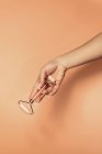 Crop anonymous female demonstrating pink quartz roller for facial skin treatment and massage against beige background — Stock Photo