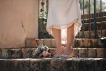 Crop mariée anonyme en robe de mariée blanche et rose chaussures peep toe à talons hauts debout près du bouquet de mariée sur les escaliers en pierre altérée — Photo de stock