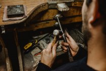 Анонимный ювелир молотит и расширяет кольцо холостым на металлической палке во время работы в мастерской — стоковое фото