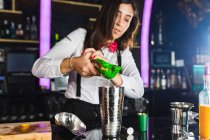 Giovane barista donna in abito elegante spremitura limone mentre si prepara cocktail in piedi al bancone in bar moderno — Foto stock