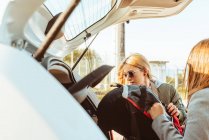 Frauen in Mänteln packen Taschen in den Kofferraum des Autos und bereiten sich gemeinsam auf eine Autofahrt vor — Stockfoto