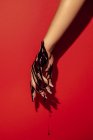 Cortar fêmea irreconhecível com manicure e fluxos de tinta preta na mão sobre fundo vermelho com sombra — Fotografia de Stock