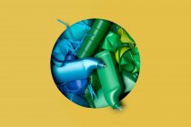 Разнообразные разноцветные пластиковые пакеты, проходящие через отверстие на желтом фоне — стоковое фото