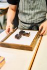 Обрізати невпізнаваного майстра чоловічої статі, що працює з металевими літерами в дерев'яній рамці, стоячи за столом в типографії — стокове фото