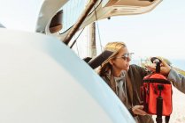 Donne in cappotti mettendo borse nel bagagliaio di auto che si preparano per il viaggio insieme — Foto stock