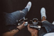 From above crop hands of people in casual wear and white sneakers holding vintage camera on blurred background — Stock Photo