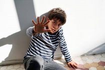Unzufriedener preteen ethnischer Junge sitzt auf dem Boden und streckt den Arm aus, während er versucht, sich vor wütenden Eltern zu schützen — Stockfoto