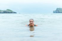 Mulheres idosas ativas de cabelos grisalhos nadando na água do oceano enquanto desfrutam do verão e praticam um estilo de vida saudável na costa — Fotografia de Stock