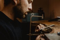Goldschmied schneidet Metall mit Säge und fertigt Schmuck in Werkstatt — Stockfoto