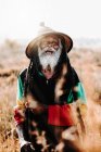 Fröhlicher alter Rastafari mit Dreadlocks, der auf einer trockenen Wiese in der Natur in die Kamera blickt — Stockfoto