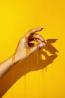 Culture femelle méconnaissable montrant la main avec manucure et des liquides de miel aromatiques sur fond jaune avec de l'ombre — Photo de stock
