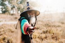 Веселое старое этническое растафари с дредами, смотрящее в камеру, стоящее на сухом лугу в природе — стоковое фото
