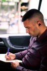 Focused Hispanic male entrepreneur sitting on passenger seat of car and writing in planner while commuting to work — Stock Photo