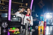 Garçonete focado feminino em roupa elegante adicionando líquido de garrafa em jigger enquanto prepara coquetel em pé no balcão no bar moderno — Fotografia de Stock
