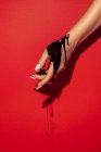 Crop unrecognizable female with manicure and black paint streams on hand on red background with shadow — Stock Photo