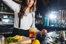 Cropped unrecognizable female barkeeper in stylish outfit liquid from bottle into glass while preparing cocktail standing at counter in modern bar — Stock Photo