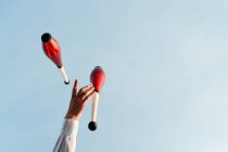 D'en bas de la récolte artiste de cirque anonyme effectuant tour avec des clubs de jonglerie contre le ciel bleu — Photo de stock
