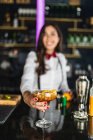 Blurred unrecognizable female barkeeper in stylish outfit serving cocktail with lemon peel while standing at counter in modern bar — Stock Photo