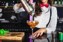 Beschnitten unkenntlich weibliche Barkeeper in stilvollem Outfit serviert Cocktail aus einem Shaker in ein Glas, während an der Theke in modernen Bar stehen — Stockfoto