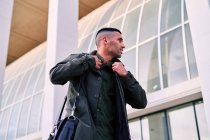 From below Hispanic male employee with briefcase smiling and looking at camera while walking on pavement near modern building in city — Stock Photo