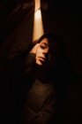 Сверху тихая молодая женщина лежит на полу в темной комнате со светящимся от открытой двери светом, глядя в камеру — стоковое фото