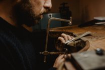Orfèvre méconnaissable coupant le métal avec une scie tout en faisant des bijoux en atelier — Photo de stock