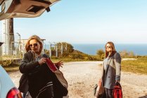 Women in coats putting bags in trunk of car preparing for road trip together — Stock Photo