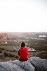 Vue pittoresque de jeune touriste assis sur le sommet de la montagne et regardant loin dans la journée ensoleillée — Photo de stock