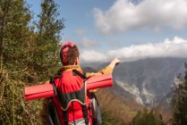 Back view of delighted female traveler with backpack standing in mountains and pointing away — Stock Photo