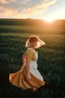 Joven hembra en vestido de estilo rústico vintage corriendo sola en el vasto campo verde herboso en la noche de verano en el campo - foto de stock