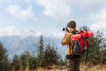 Vista lateral de la mochilera femenina tomando fotos del paisaje montañoso durante el viaje - foto de stock