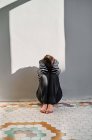 Unerkennbares unglückliches Kind, das auf dem Boden sitzt und den Kopf mit den Händen bedeckt, während es zu Hause unter häuslicher Gewalt leidet — Stockfoto