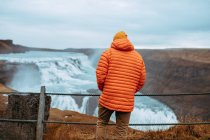 Indietro vista del giovane turista in inverno indossare guardando cascata e fiume di montagna tra pietra collina — Foto stock