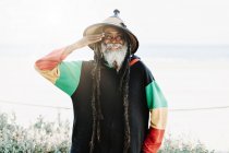 Portrait of cheerful old ethnic rastafari with dreadlocks looking at the camera in the nature with white background — Stock Photo