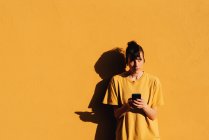 Mulher contemporânea com corte de cabelo elegante e piercing usando smartphone em mídias sociais contra fundo amarelo — Fotografia de Stock