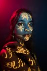 Modelo feminino jovem na moda com projeção de luz em forma de hieróglifos orientais olhando para a câmera no estúdio escuro com iluminação vermelha — Fotografia de Stock