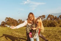 Ridendo donna bionda dando cavalcata a fidanzate allegre in possesso di sapone bastone bolla camminare in natura — Foto stock