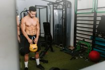 Спортивный мужчина с обнаженным туловищем делает упражнения с тяжелыми гирями во время активных тренировок в спортивном центре — стоковое фото